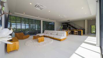 A spacious living room with a large sectional sofa, a wooden coffee table, and a round rug. There is a kitchen area with a bar and a staircase leading to an upper level.