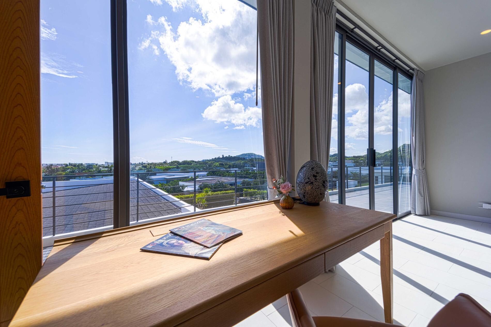 Una habitación con un ventanal amplio, un escritorio de madera y vistas a un paisaje urbano.