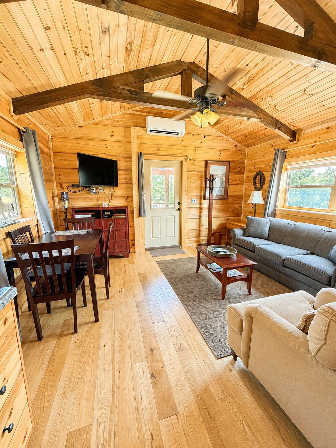 Interior de uma cabana de madeira, com área de jantar, sofá e televisão.