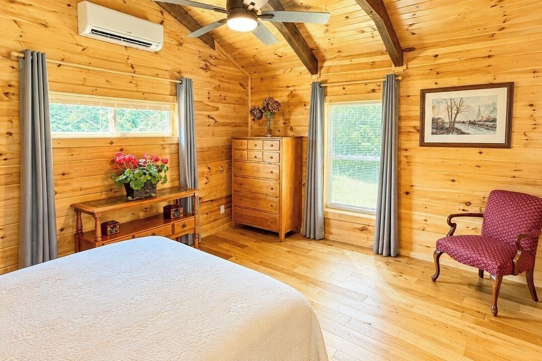Une chambre dans une cabane en bois, avec un lit, une commode, une chaise et un ventilateur de plafond.