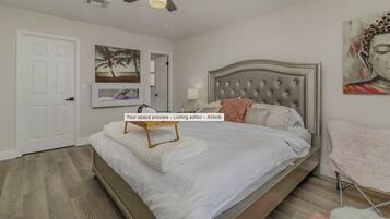 A bedroom with a bed, a ceiling fan, a door, and wall art.