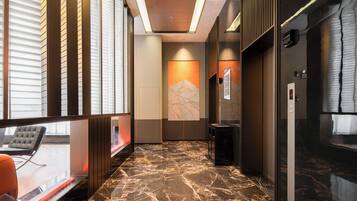 Un hall d’hôtel moderne avec un sol en marbre, un coin salon avec un canapé et une œuvre d’art accrochée au mur.