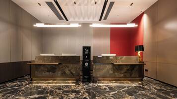 A hotel reception area with marble flooring, a reception desk, a red curtain, and a black lamp.