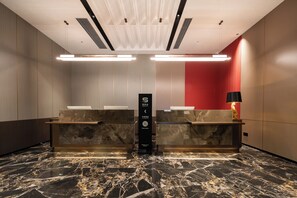 A hotel reception area with marble flooring, a reception desk, a red curtain, and a black lamp. - Licheng Donggu Hotel (Cangzhou)