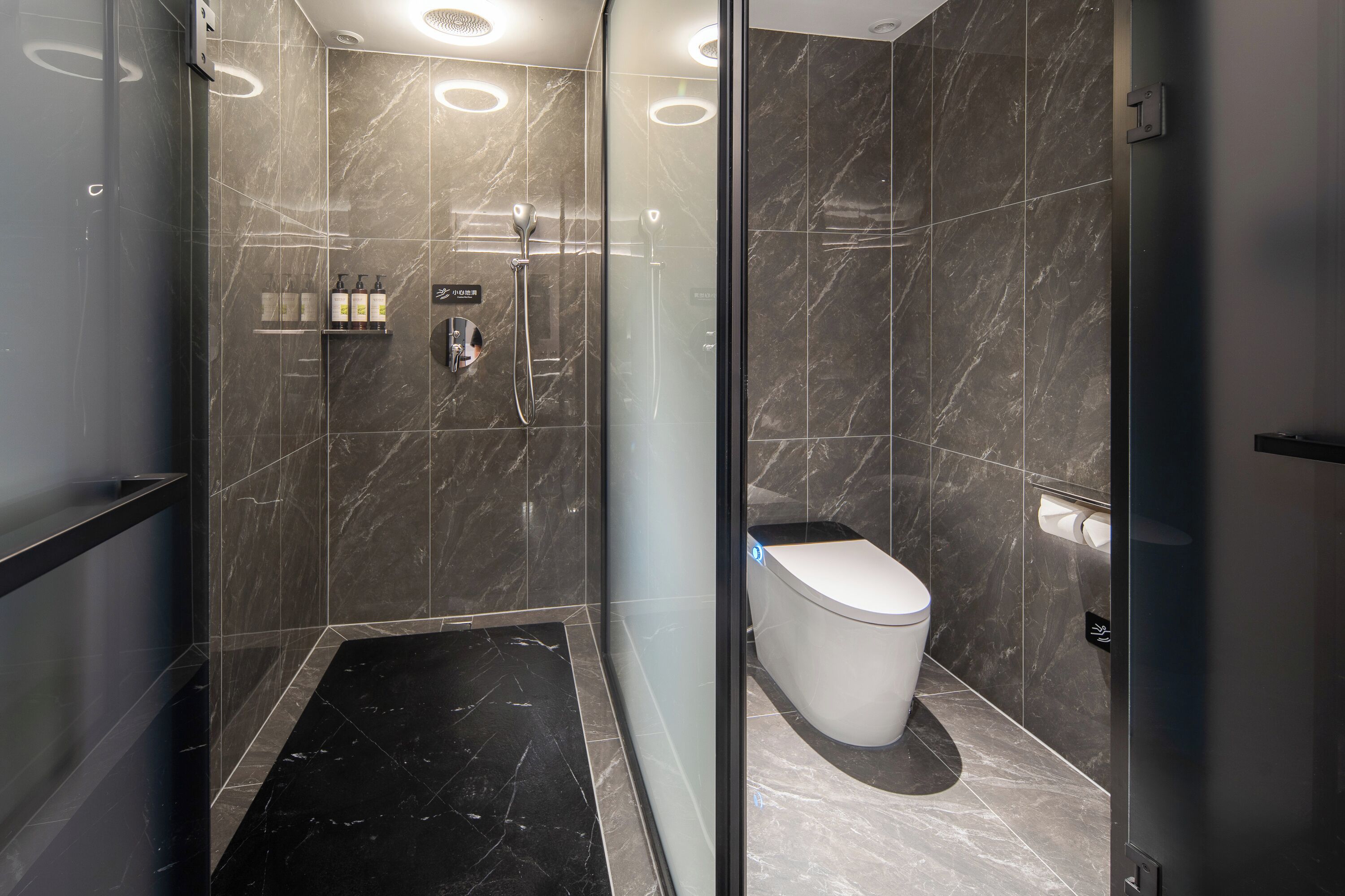 A modern bathroom with a glass-enclosed shower, a toilet, and a shelf with toiletries.
