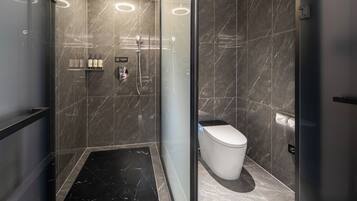 A modern bathroom with a glass-enclosed shower, a toilet, and a shelf with toiletries.