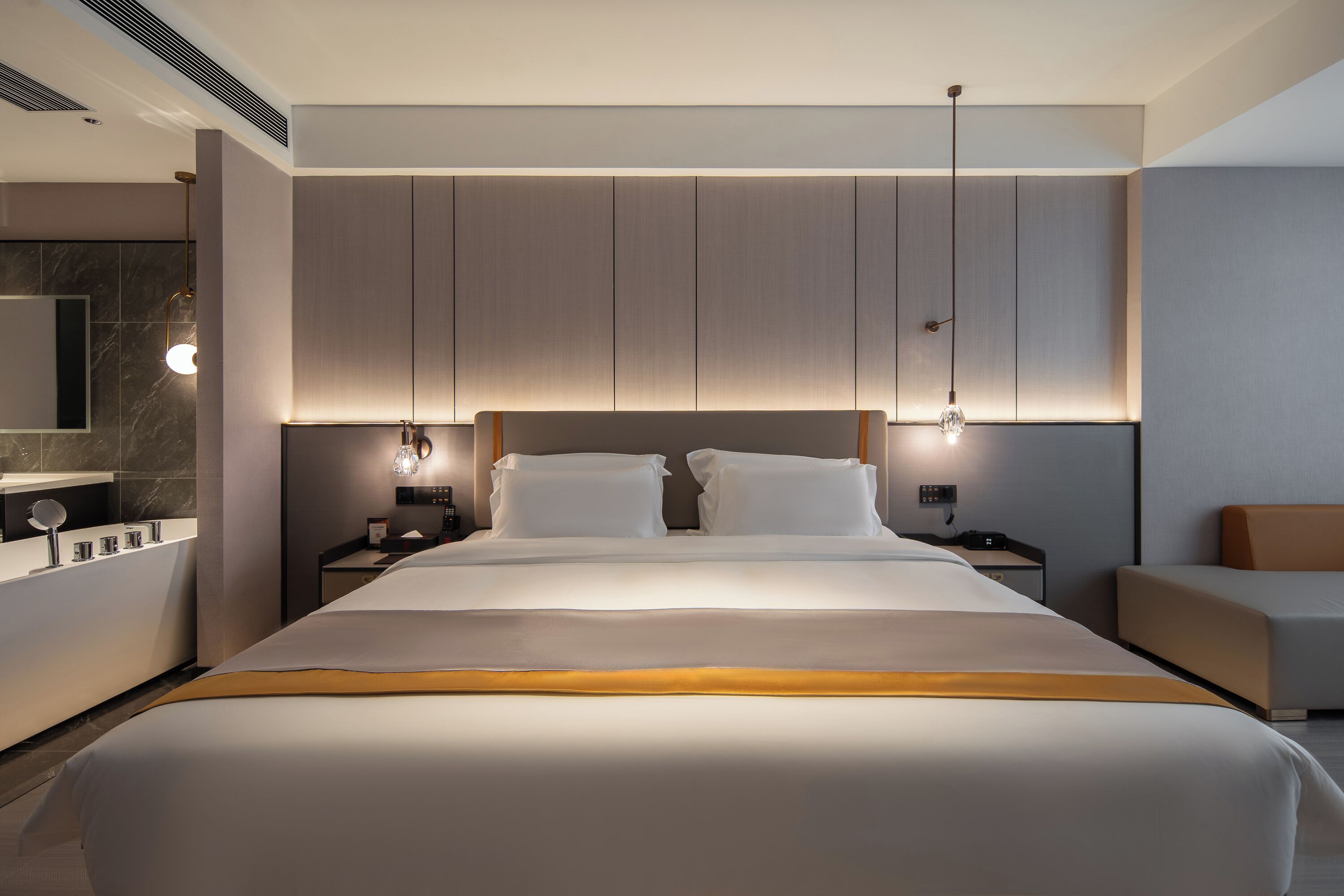 Habitación de hotel moderna con una cama grande, mesitas de noche, un escritorio, una silla y un espejo amplio.