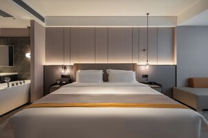 Habitación de hotel moderna con una cama grande, mesitas de noche, un escritorio, una silla y un espejo amplio.