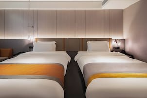 Habitación de hotel con dos camas, una mesita de noche y un panel de control en la pared.
