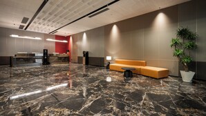 Un vestíbulo moderno con piso de mármol, una mesa de recepción, una zona de estar y una planta en maceta.
