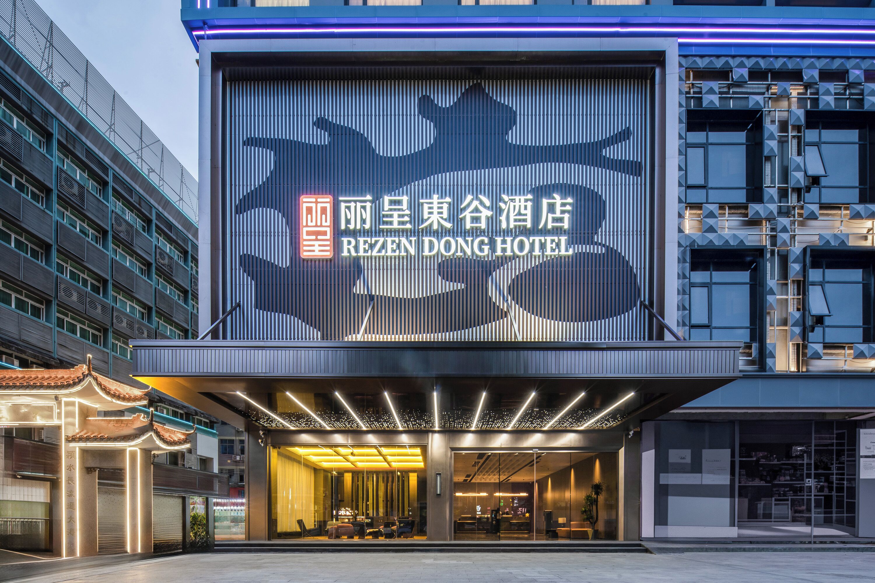 Un hotel con un gran cartel iluminado, una entrada moderna y un elemento arquitectónico tradicional.