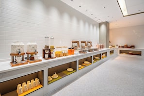 A modern cafe with a long counter, coffee machines, and a variety of food and drink containers.