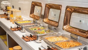 Un bufé con varias estaciones de comida, que incluyen pasta, arroz y verduras.