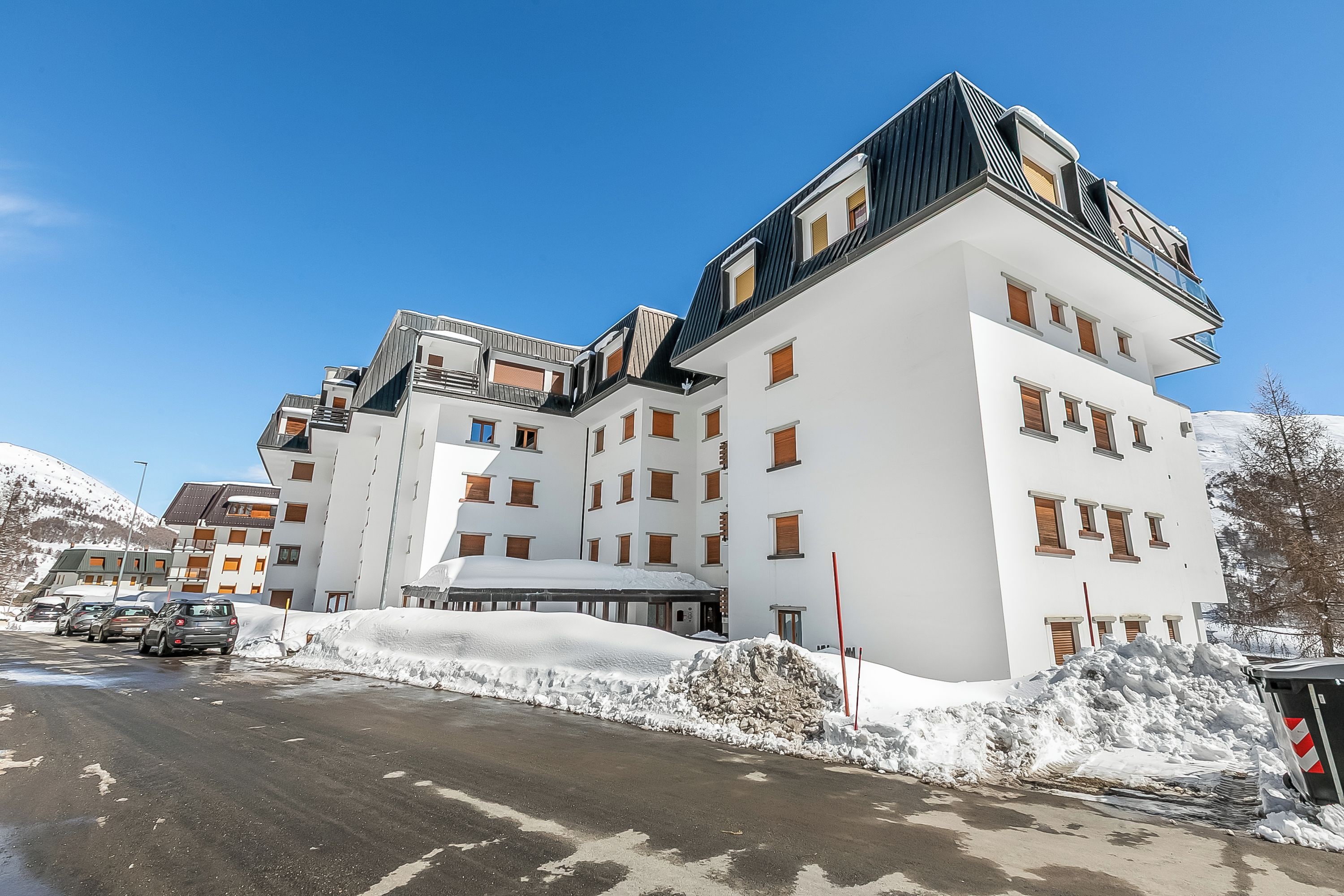 Ein mehrstöckiges Hotel mit moderner Architektur, mit Balkonen und einer Skipiste im Hintergrund.