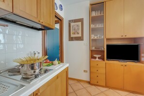 Eine kleine Küche mit Holzausstattung, einem eingebauten Herd und einem Flachbildfernseher.