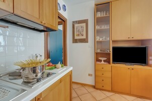 Cozinha compacta com armários de madeira, fogão embutido e televisão de tela plana.