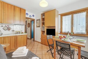 Cocina compacta con armarios de madera, zona de comedor con mesa y sillas, y ventana con cortinas.