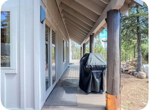 A covered outdoor area with a grill, wooden deck, and a view of trees.