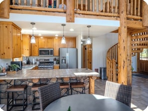 A kitchen with wooden cabinets, a stone island, and a dining area with wicker chairs.