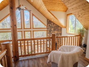 A wooden deck with a stone wall, a white fluffy chair, and a view of trees.