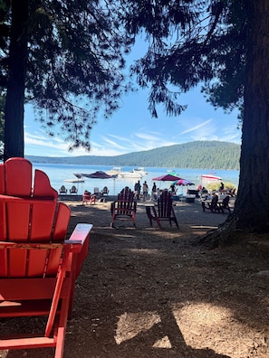 A beach with red chairs and umbrellas, a lake, and a forested hill in the background.
