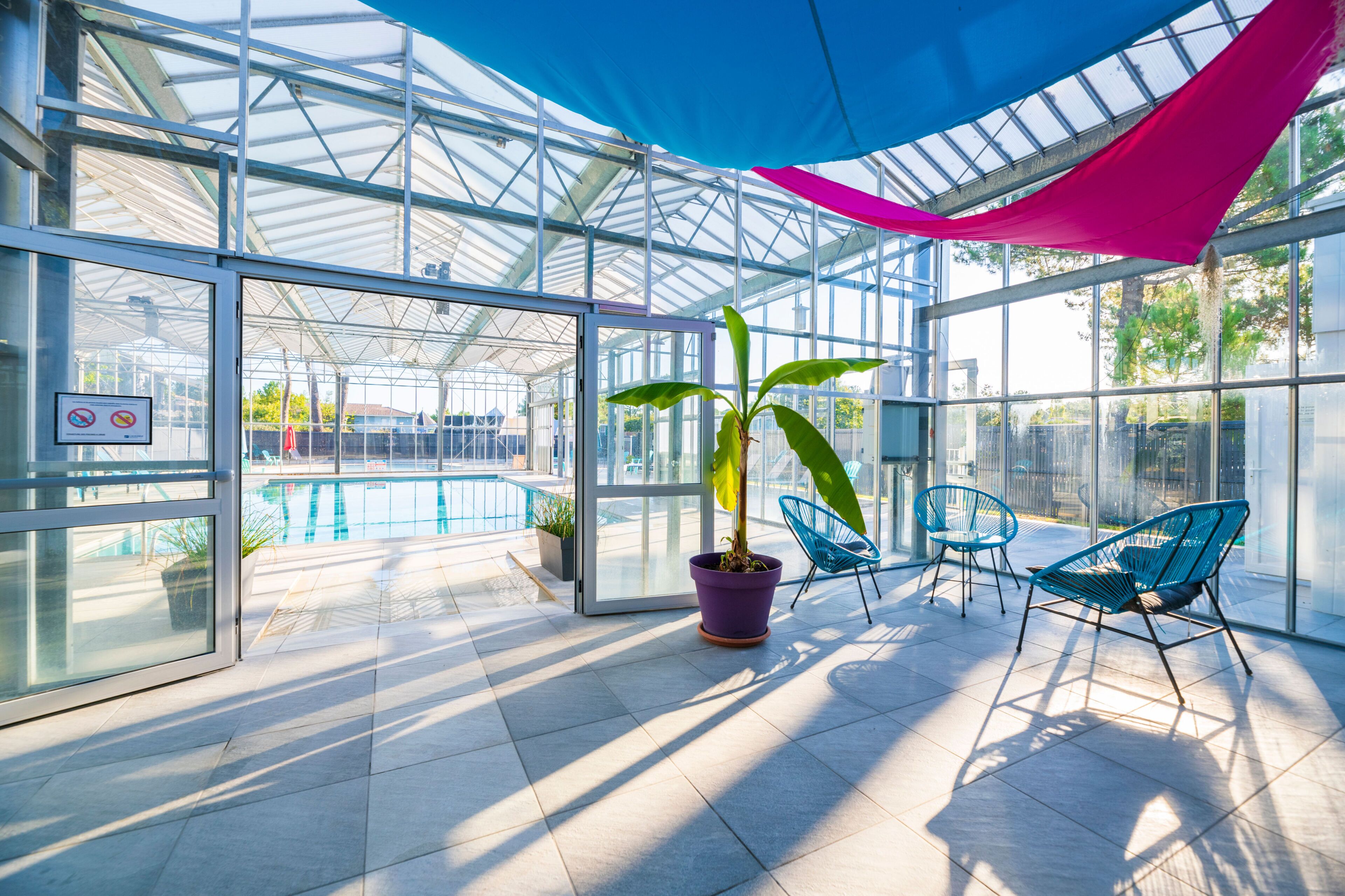 Et glasindhegnet område med pool, stole og potteplanter.