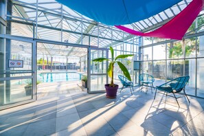 Et glasindhegnet område med pool, stole og potteplanter.