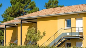 Um edifício amarelo com telhado em telhas, uma escadaria e uma pequena janela.
