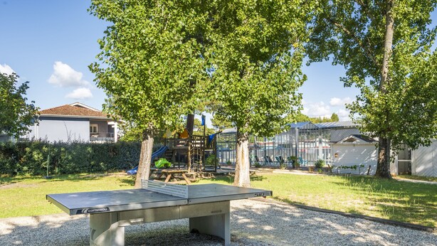 Uma mesa de pingue-pongue em um parque, com brinquedos e casas ao fundo.