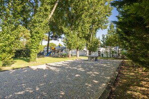 Ein Spielplatz mit Rutschen und einem Picknicktisch, umgeben von Kies und Bäumen.