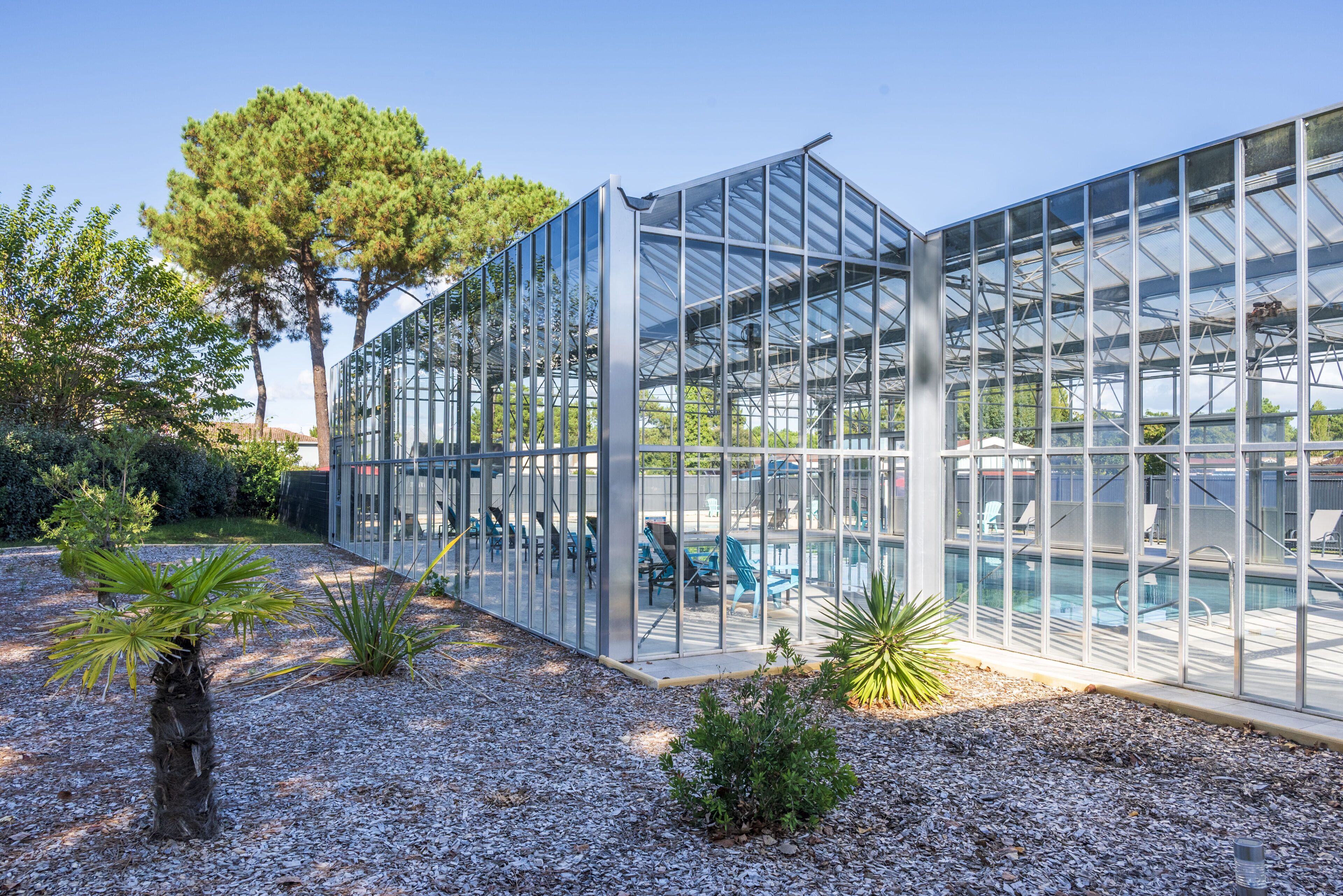 A modern glass greenhouse structure with a pool area visible through the transparent walls.