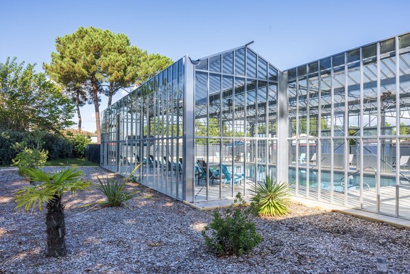 A modern glass greenhouse structure with a pool area visible through the transparent walls.
