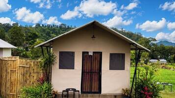 Uma casa térrea com telhado plano, porta frontal e um pequeno alpendre com duas cadeiras e uma mesa.