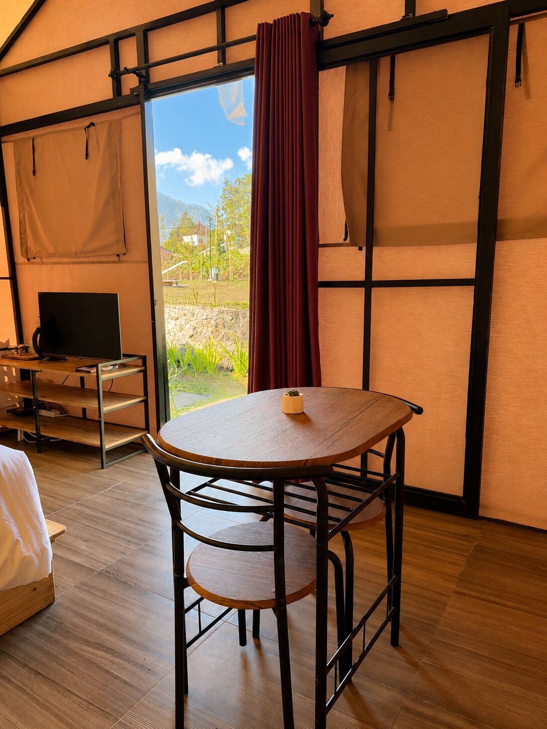Una habitación con una mesa redonda, una silla, una cama, un televisor y vistas al exterior.