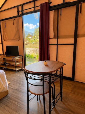 Una habitación con una mesa redonda, una silla, una cama, un televisor y vistas al exterior.
