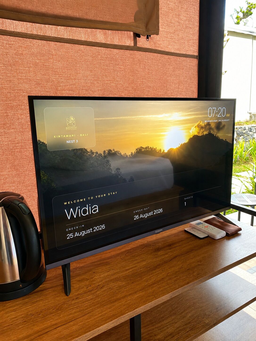 A television displaying a sunset view, a check-in/out date, and a guest count.