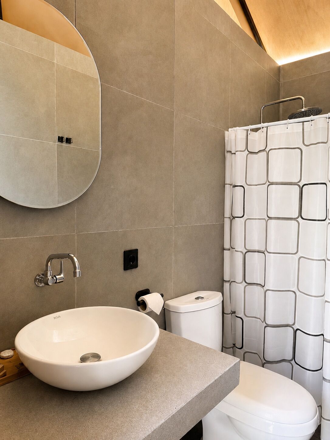 Een moderne badkamer met een rond wastafel, toilet en een douchegordijn met een geometrisch patroon.