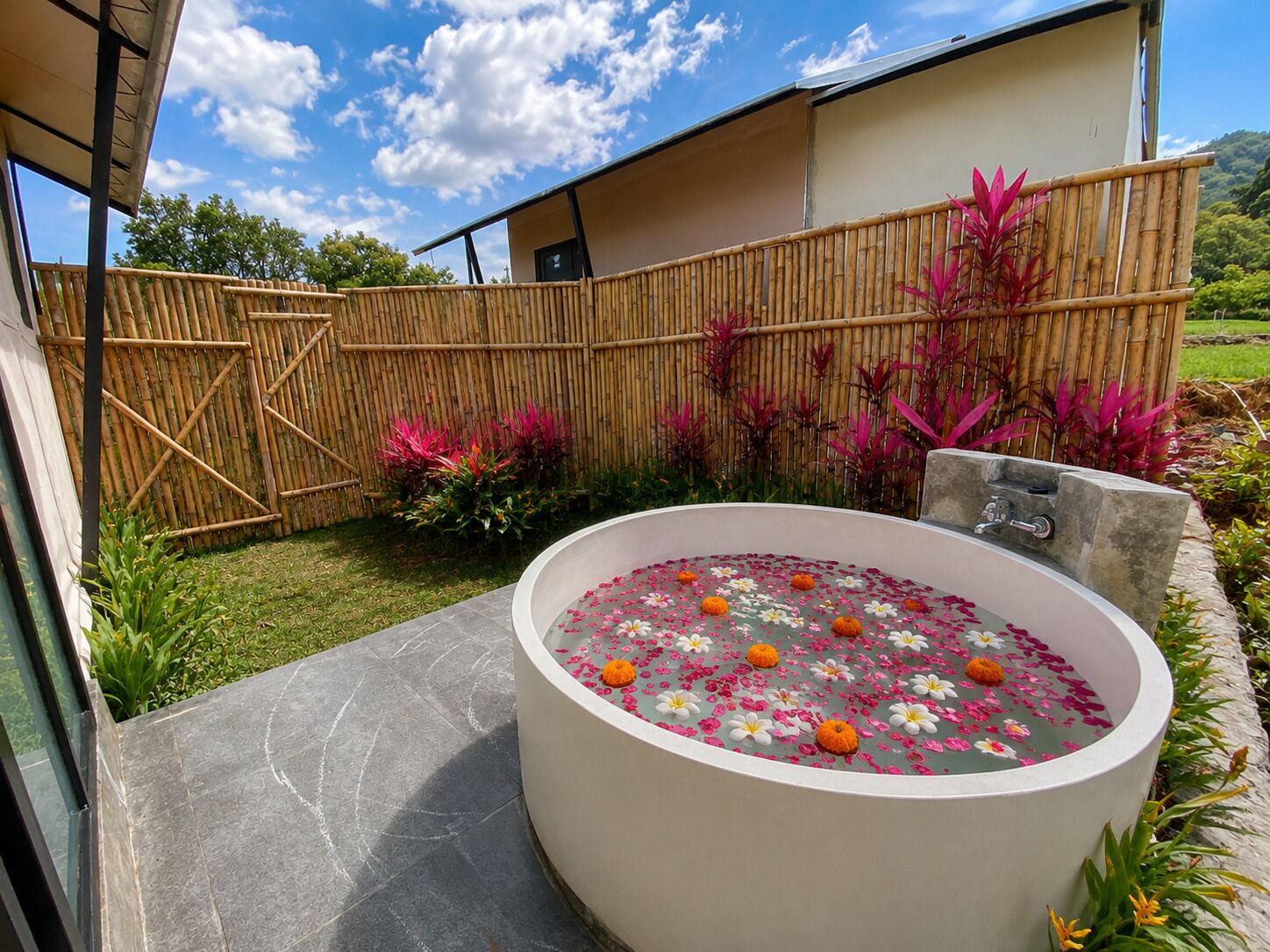 Uma área de spa com hidromassagem, cercada por um mureta de bambu e plantas tropicais.