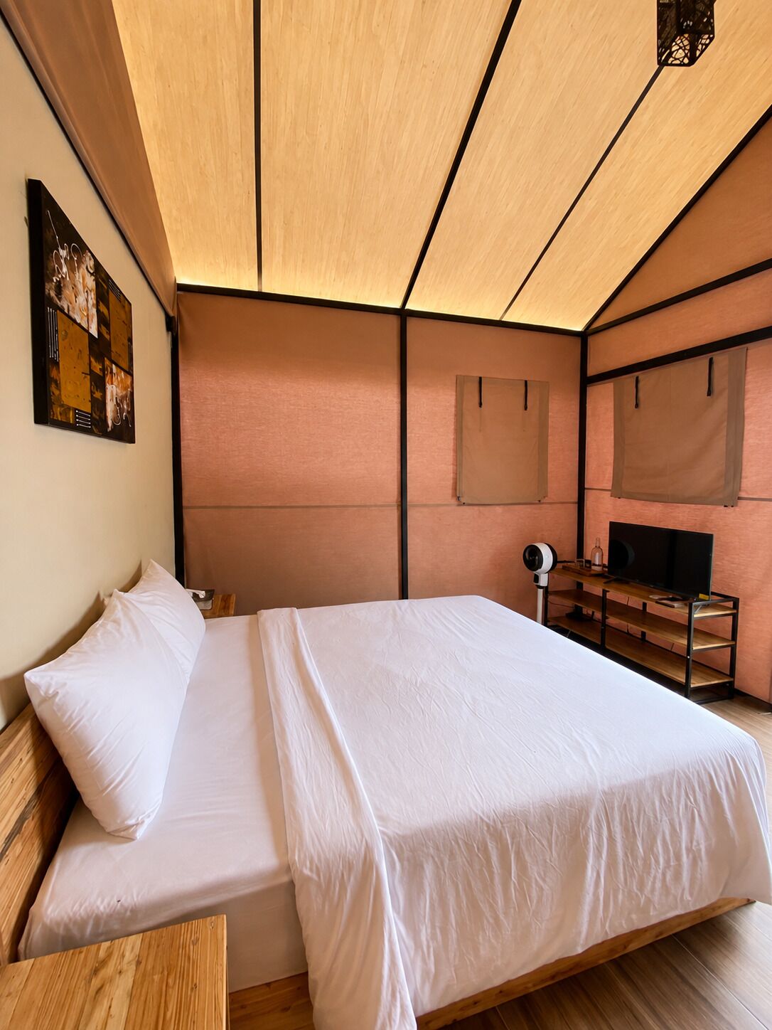 A bedroom with a bed, a wooden nightstand, a television on a wooden stand, and a wall-mounted lamp.
