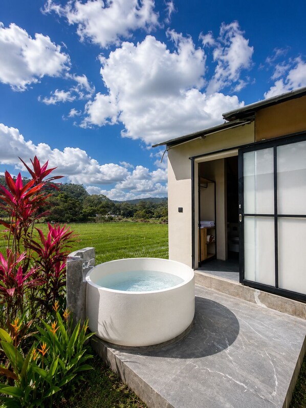 Un edificio moderno con jacuzzi, puerta de vidrio y vistas a un campo verde.