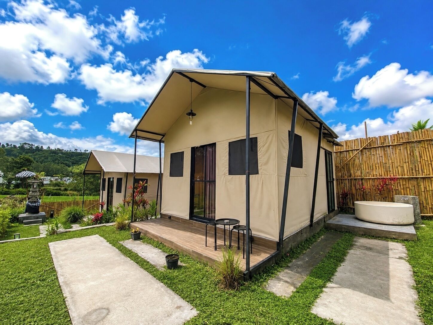 A single-story, beige-colored house with a porch, a small garden, and a bamboo fence.