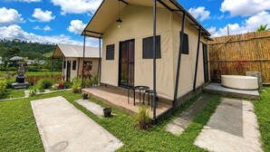 A single-story, beige-colored house with a porch, a small garden, and a bamboo fence.