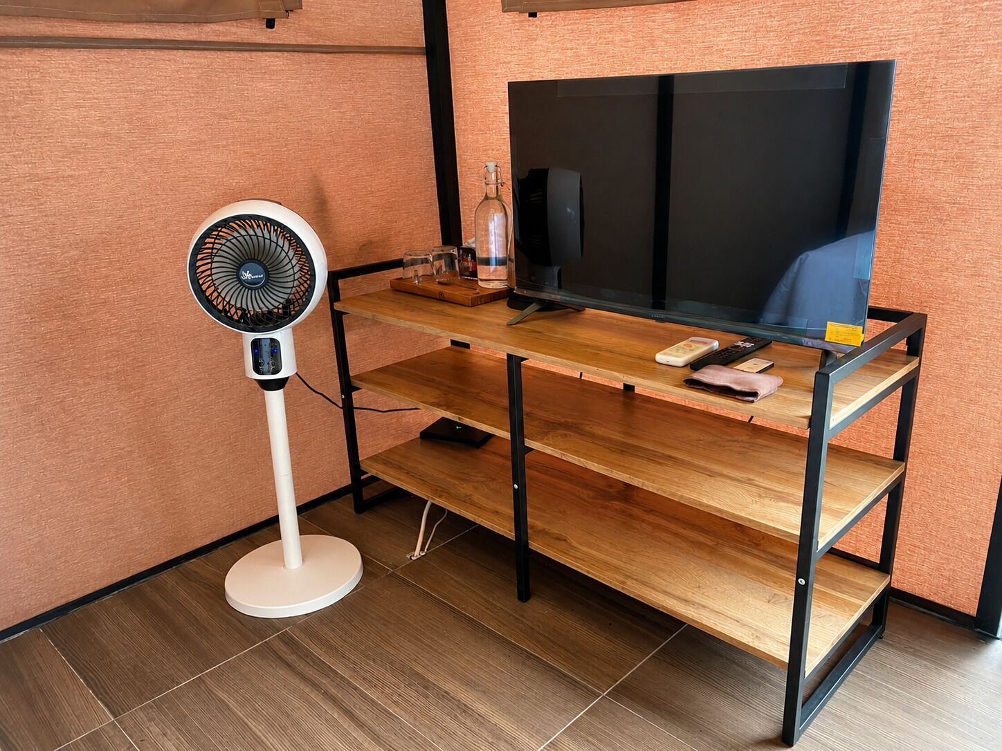 A wooden desk with a television, a fan, and a bottle.