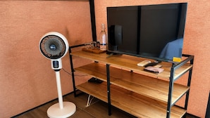 A wooden desk with a television, a fan, and a bottle.