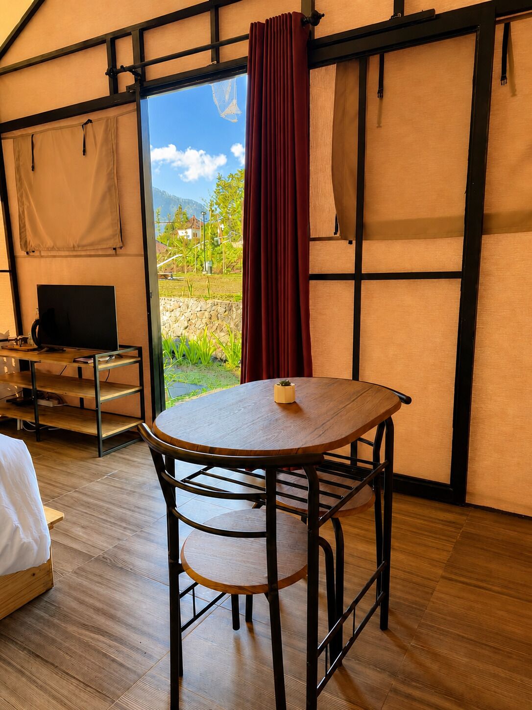 Una habitación con cama, una mesa con silla, televisión y vistas al exterior.