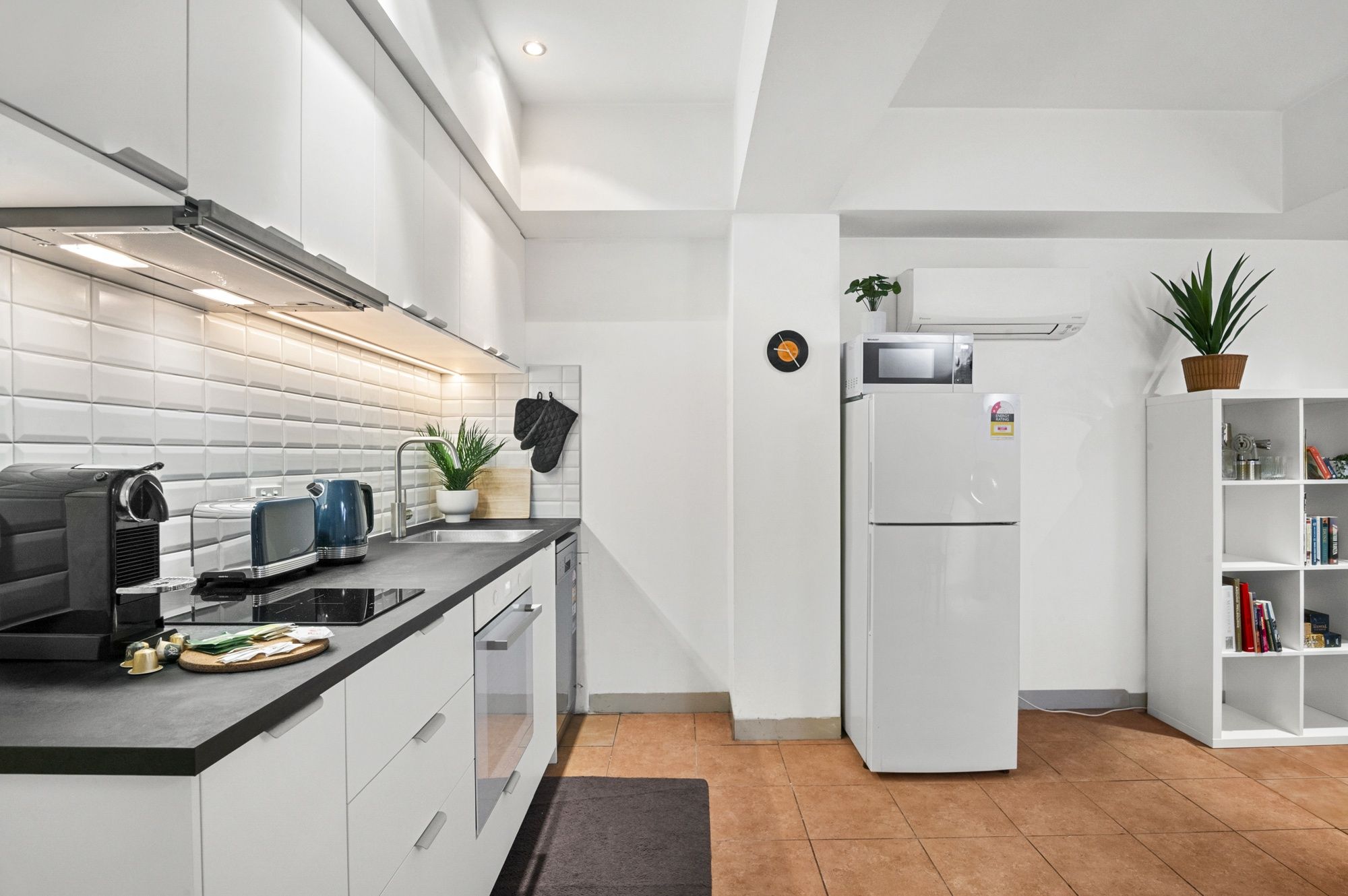 Eine moderne Küche mit weißen Schränken, einer schwarzen Arbeitsplatte, einem eingebauten Backofen und einem weißen Kühlschrank.