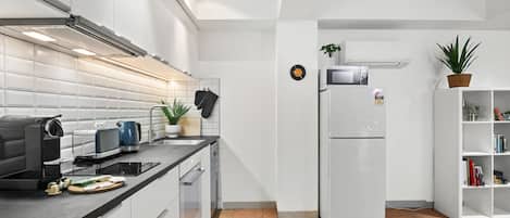 Eine moderne Küche mit weißen Schränken, einer schwarzen Arbeitsplatte, einem eingebauten Backofen und einem weißen Kühlschrank.
