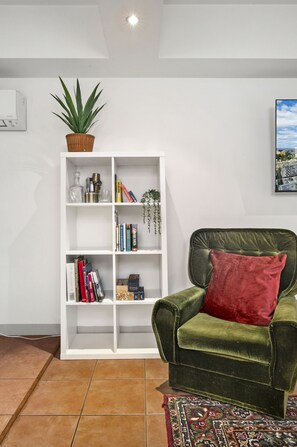 A living room with a green velvet armchair, a white bookshelf, and a patterned rug. - Melbourne 1-Bed Apartment Flinders Street (Melbourne)