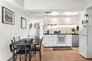 A modern kitchen with white cabinets, a black dining table, and chairs, a built-in oven, and a microwave. - Melbourne 1-Bed Apartment Flinders Street (Melbourne)