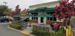 Um Starbucks com área externa, fachada de tijolos e um estacionamento ao fundo.